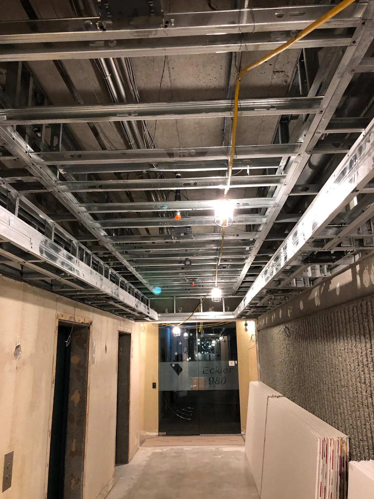 Overhead steel ceiling grid framing in the Eckler 980 elevator lobby, glass entry doors visible ahead