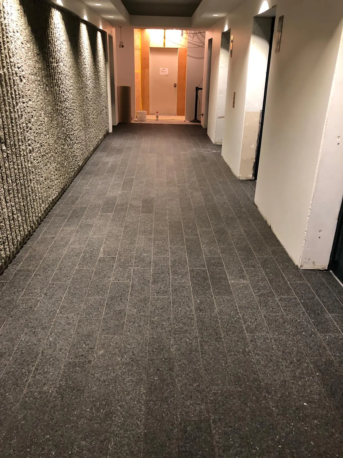 Finished elevator corridor with dark tile flooring and a textured stone feature wall