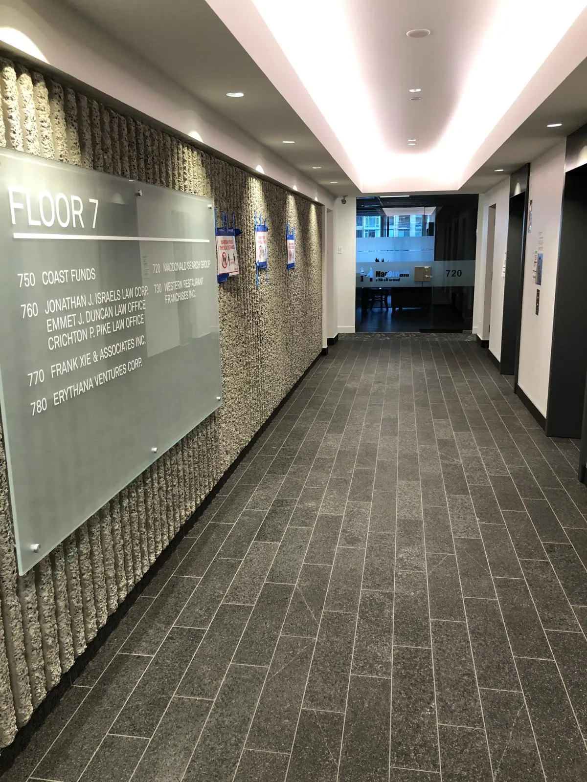 Finished Floor 7 corridor with a tenant directory sign against the same textured feature wall and dark tile flooring