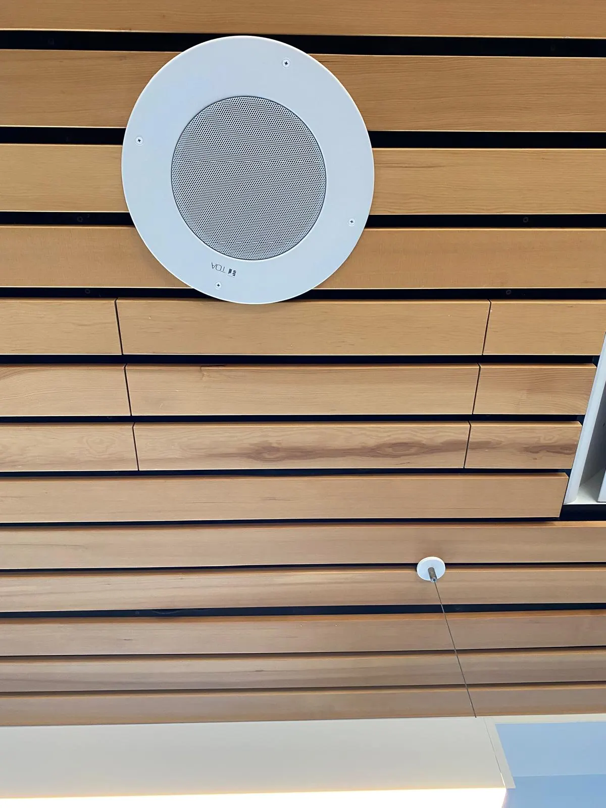 Close-up of the finished wood slat ceiling detail with a recessed speaker and lighting fixtures