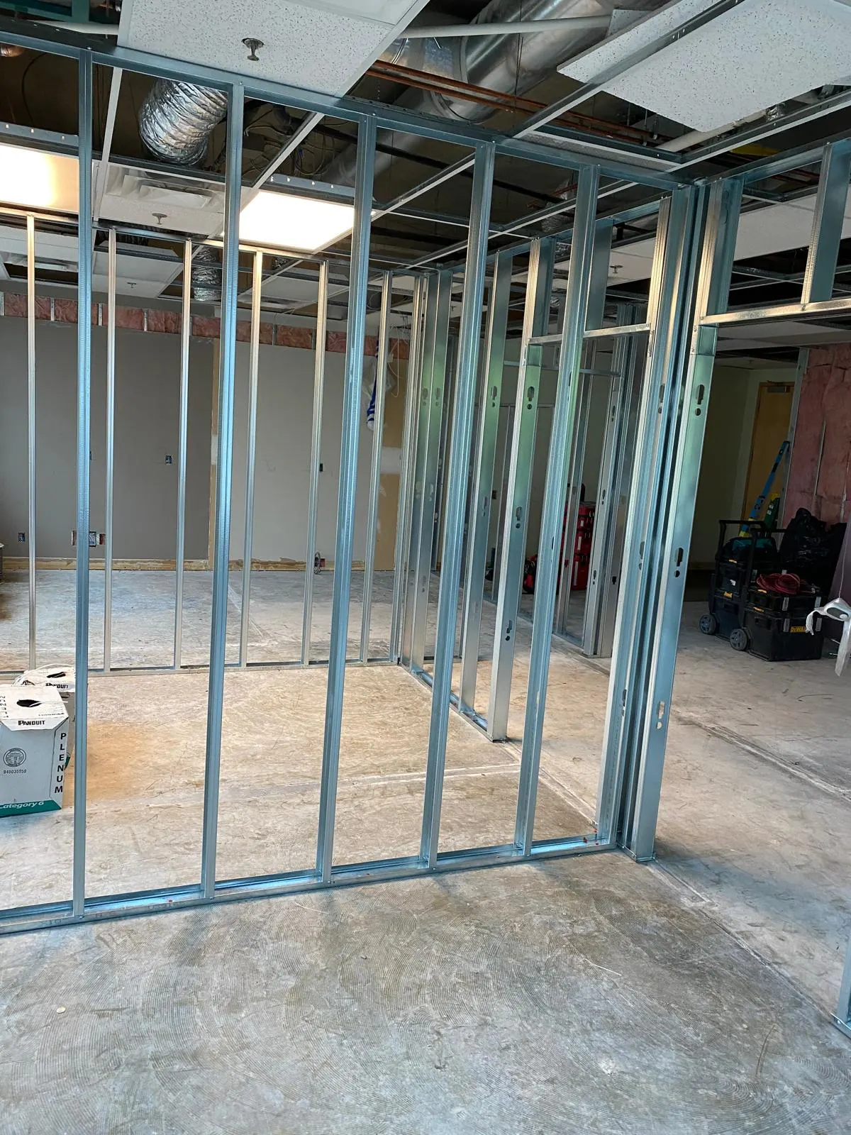 Steel-stud partition framing for a commercial office interior, door openings roughed in, ceiling tile and ductwork exposed above