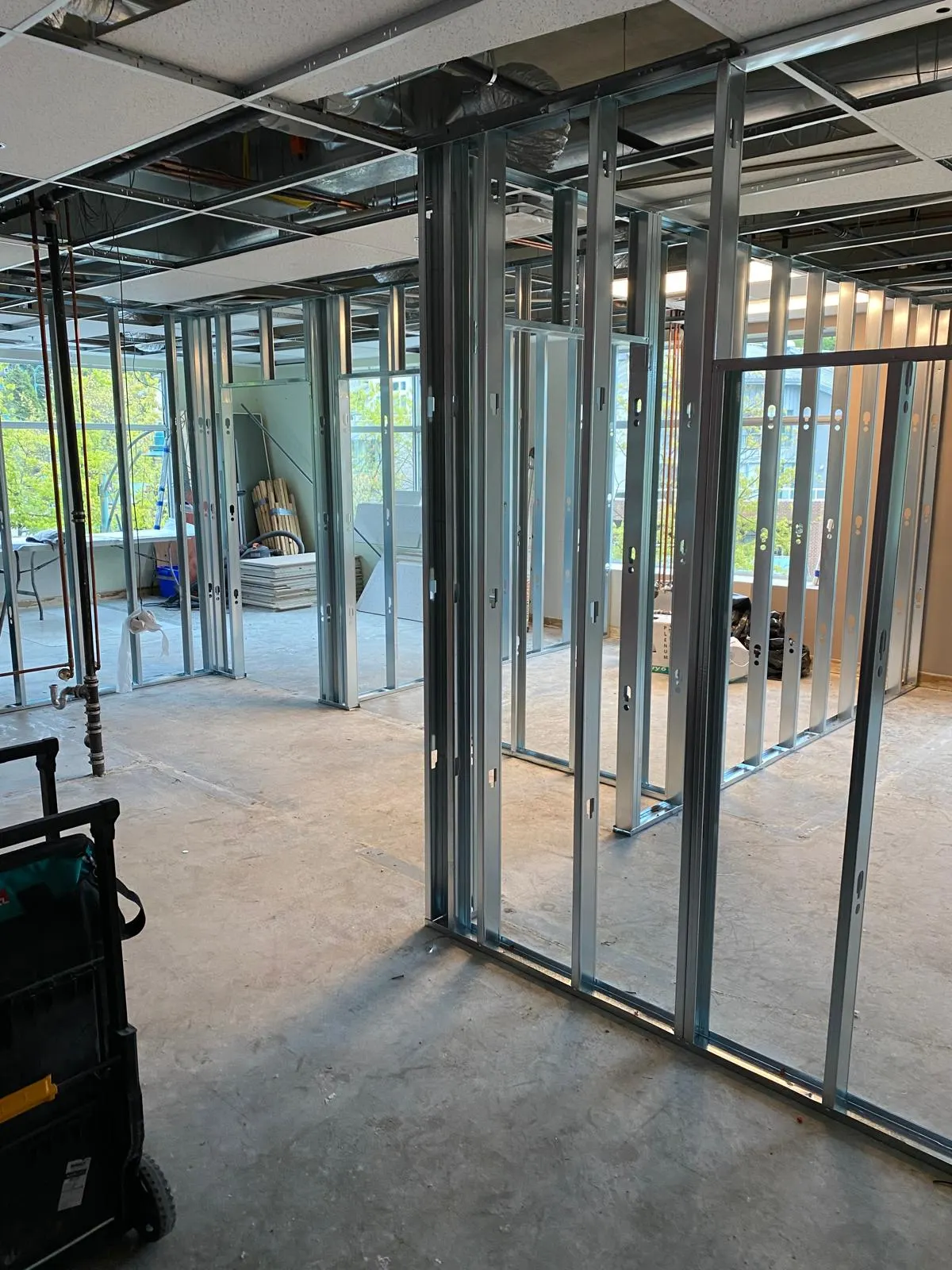 New steel-stud partition framing dividing rooms in a gutted office suite, tool carts staged in the foreground