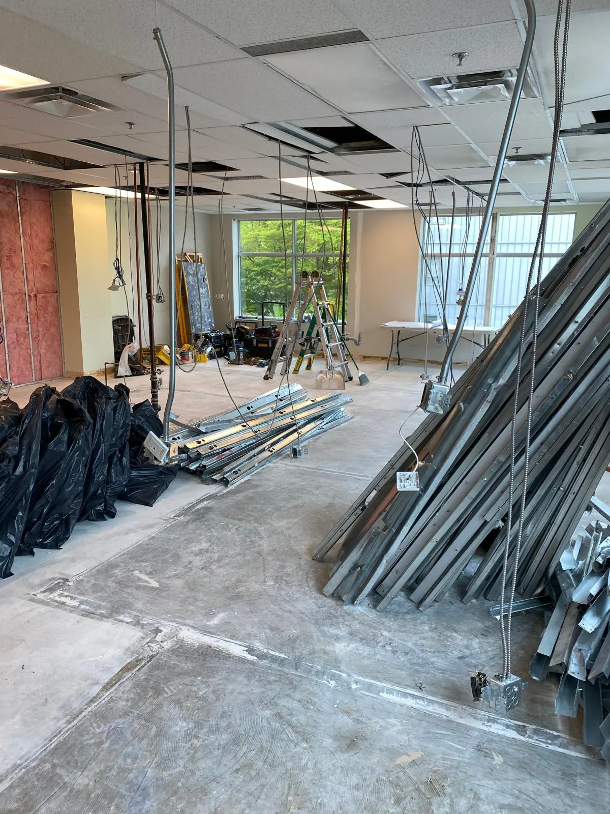 Bundled steel studs and demolition bags staged in a gutted office space with pink insulation exposed on one wall