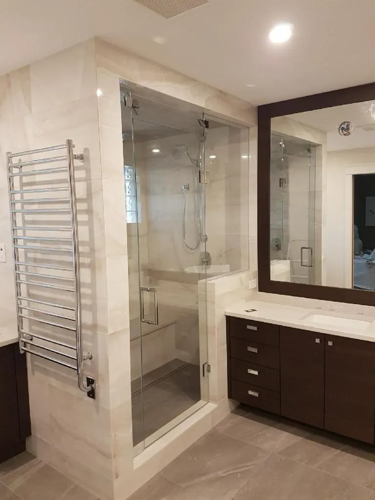 Finished marble tile bathroom with a glass shower enclosure, heated towel warmer, and dark wood vanity