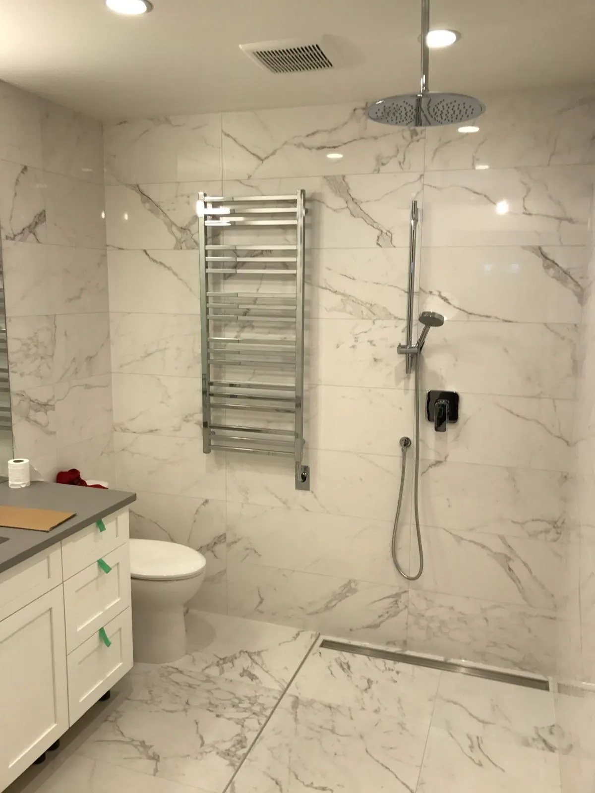 Finished marble tile bathroom with a rain shower head, heated towel warmer, and white vanity