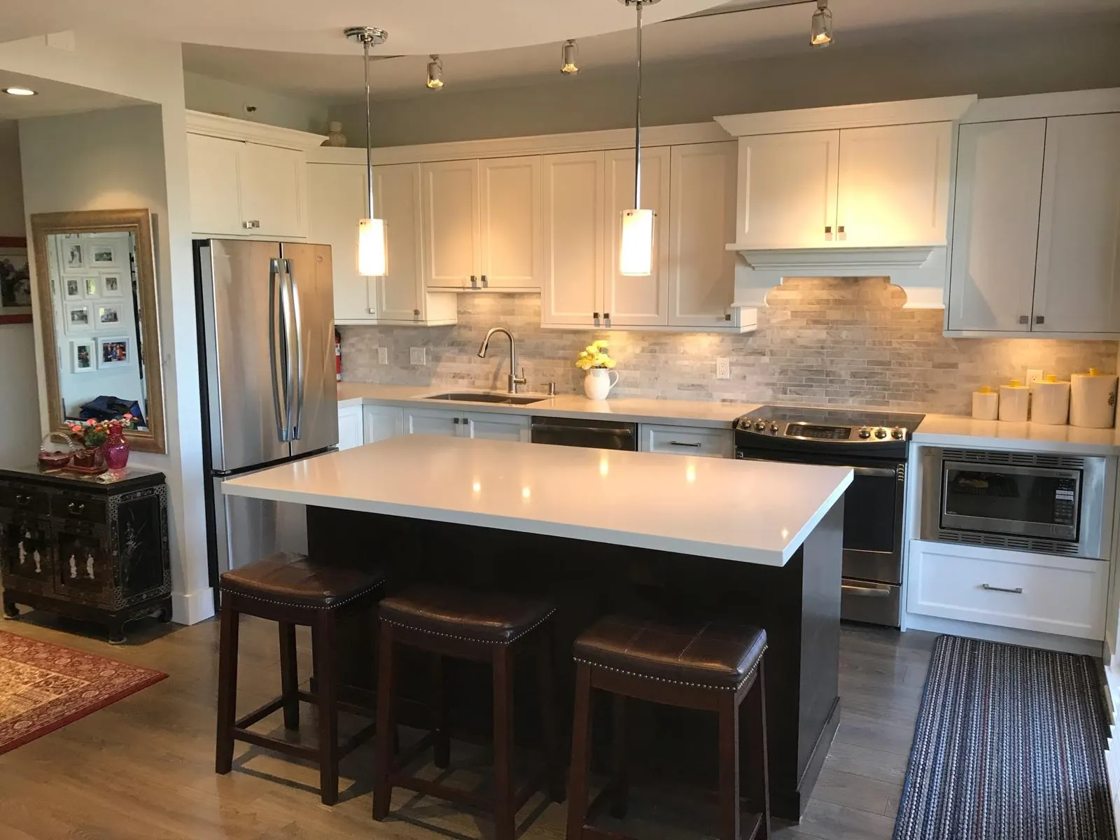 The same kitchen seen from a different angle, showing the full run of white cabinets and stacked-stone backsplash