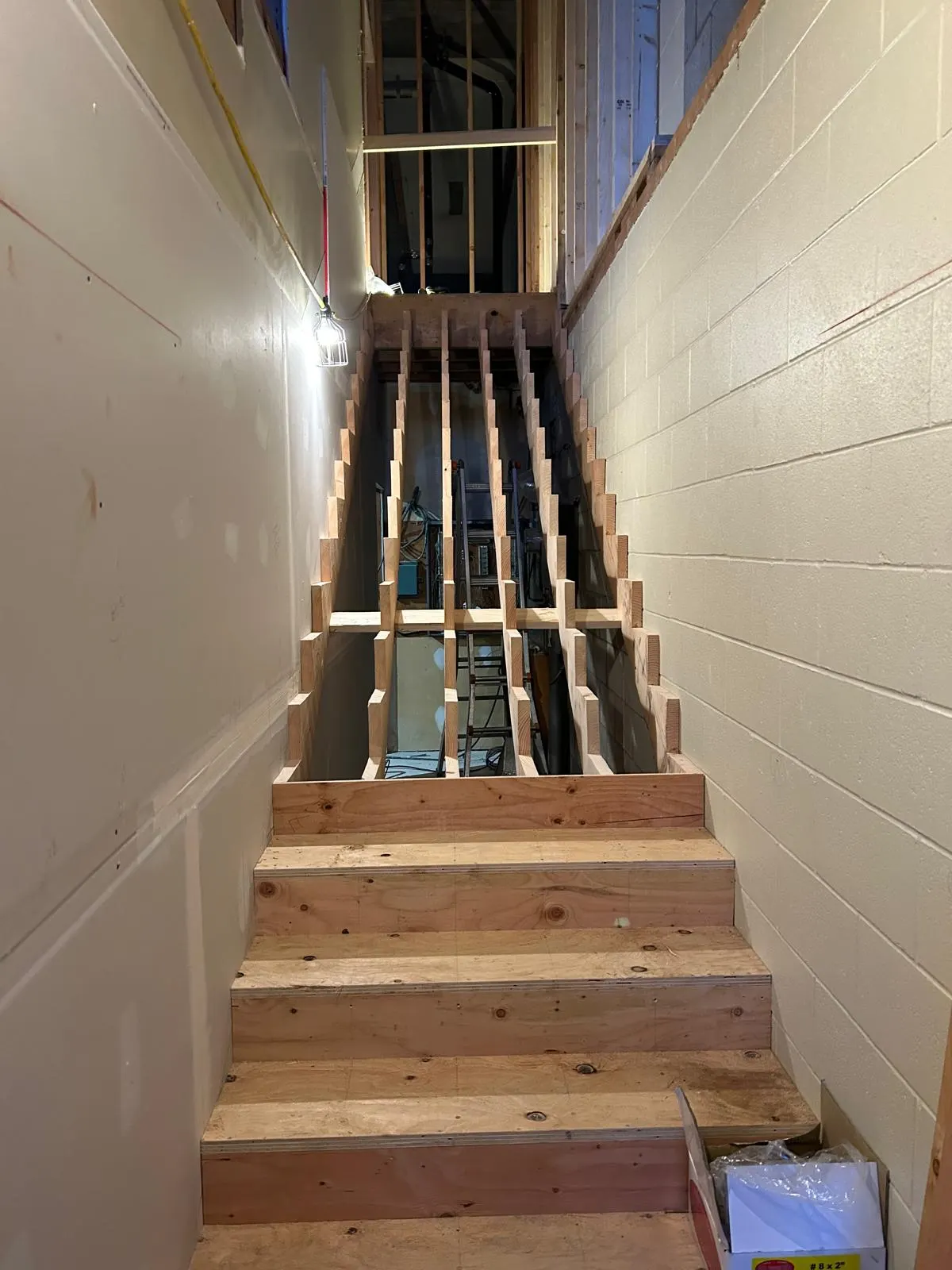 Wood-framed basement stairwell under construction between a concrete block wall and new drywall