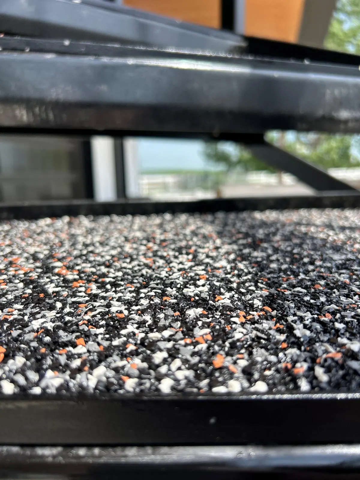 Close-up macro shot of a rubberized stair tread showing the black, white, and orange rubber granule blend