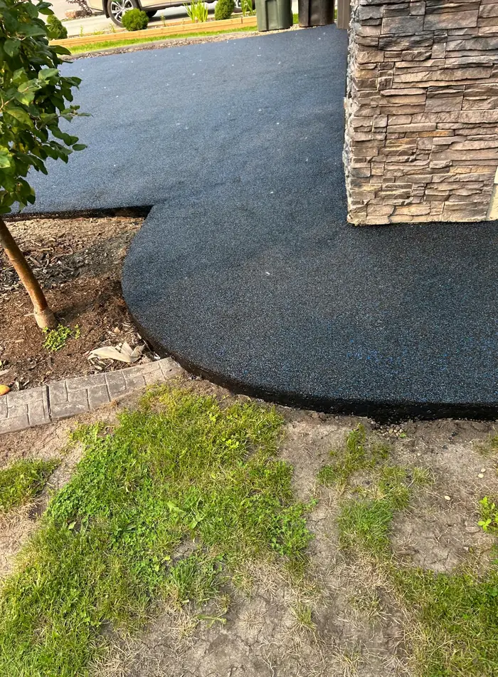 Curved edge of the poured rubber walkway where it wraps past a stone-clad pillar and a garden bed
